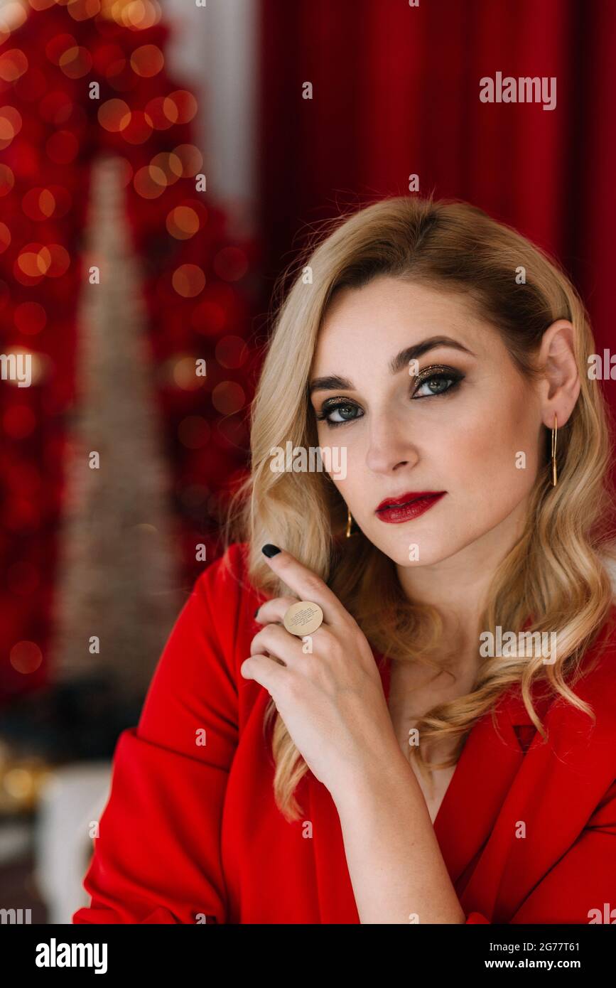 Portrait jeune belle femme blonde en rouge sur le fond des lumières bokeh d'un arbre de Noël. Bonne année 2021. Mise au point douce sélective, flou artistique Banque D'Images