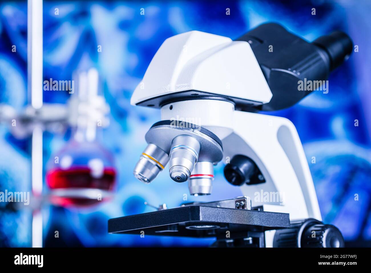 Gros plan du microscope en laboratoire avec bécher et rouge liquide flou en arrière-plan. Banque D'Images
