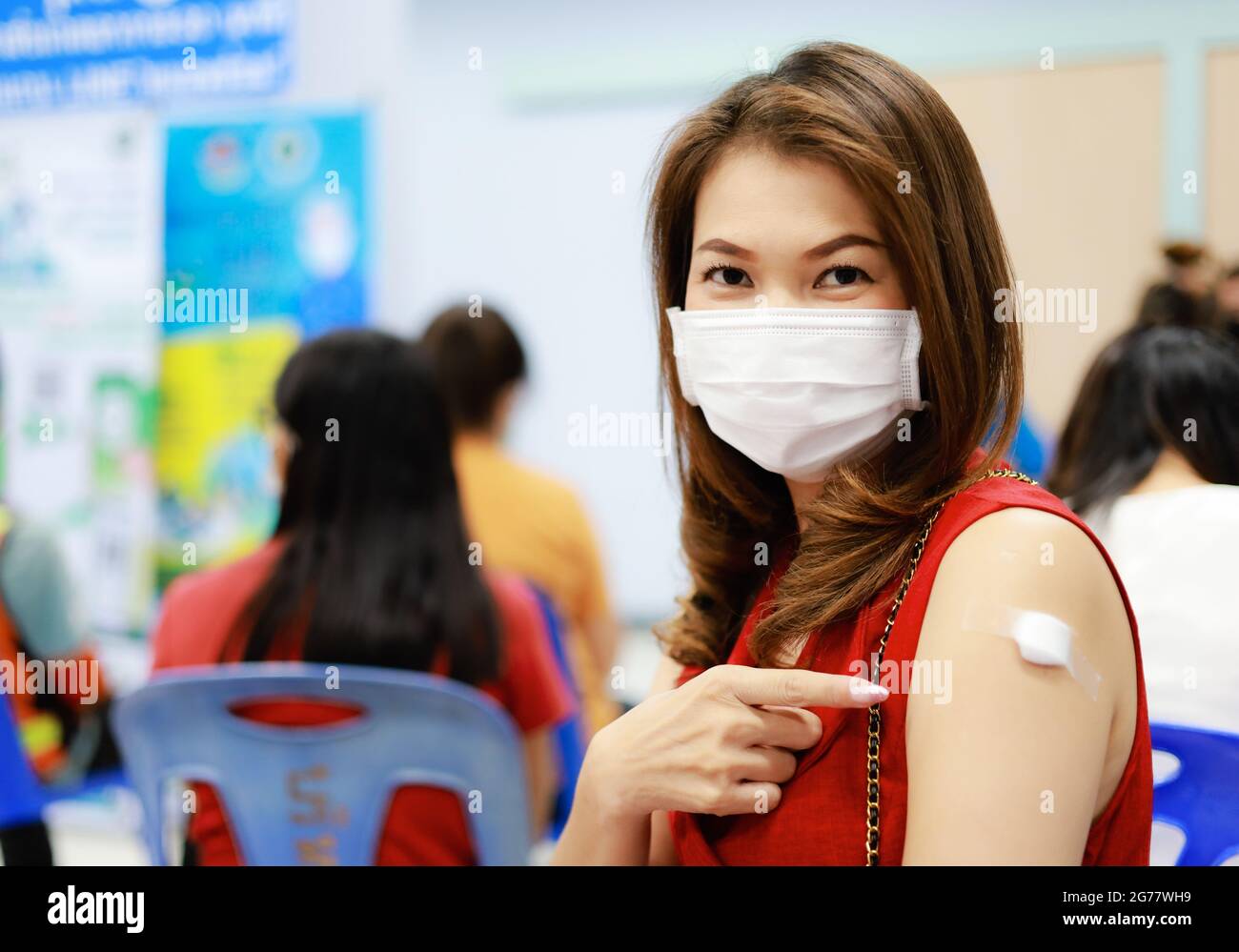 Femme asiatique portant un masque d'hygiène médicale potant le doigt sur le plâtre et le coton recouvert sur le bras après avoir reçu le vaccin contre le coronavirus ou Covid-19. Banque D'Images