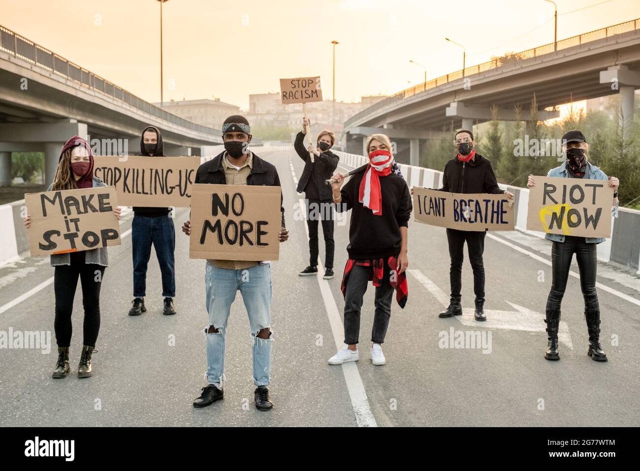 Groupe de jeunes multiethniques dans des masques en tissu debout sur la route tout en protestant dans la rue Banque D'Images