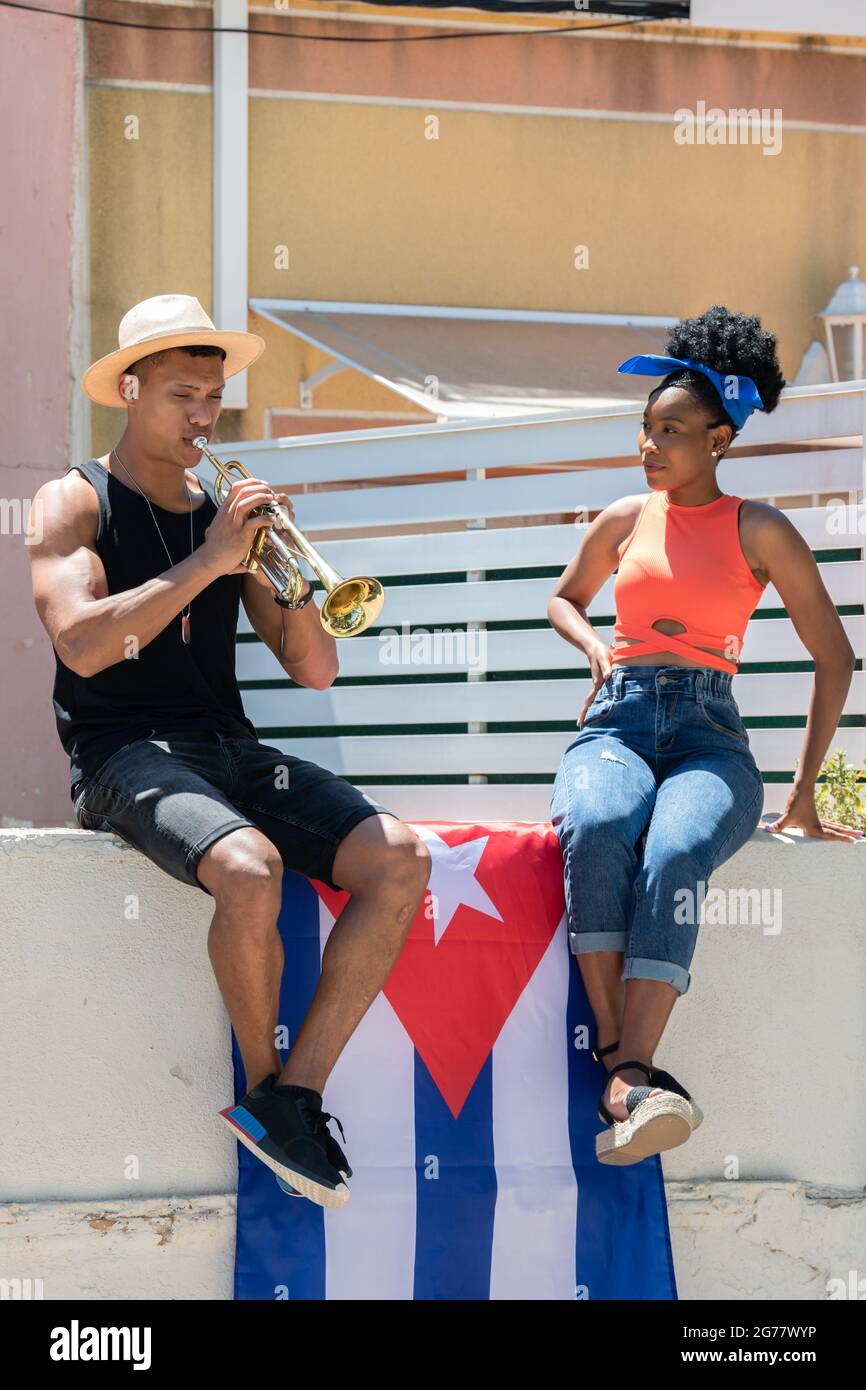 Latina femme regardant un homme latino jouer une trompette assis sur un mur  avec le drapeau cubain:Music concept Photo Stock - Alamy