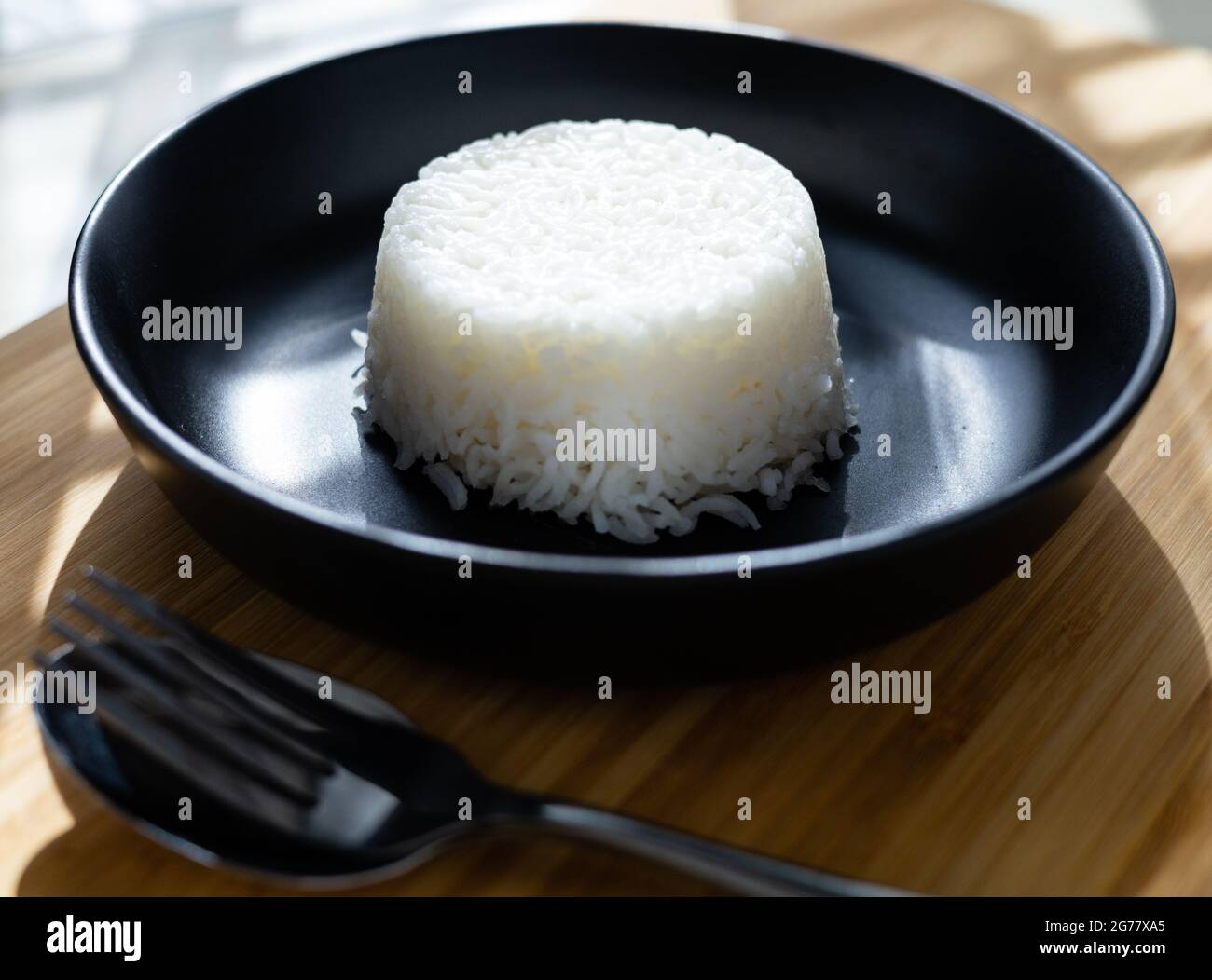 Cuisson de style thaïlandais riz vapeur mis sur plaque noire sur fond de bois avec paire de fourchette à couverts. Banque D'Images