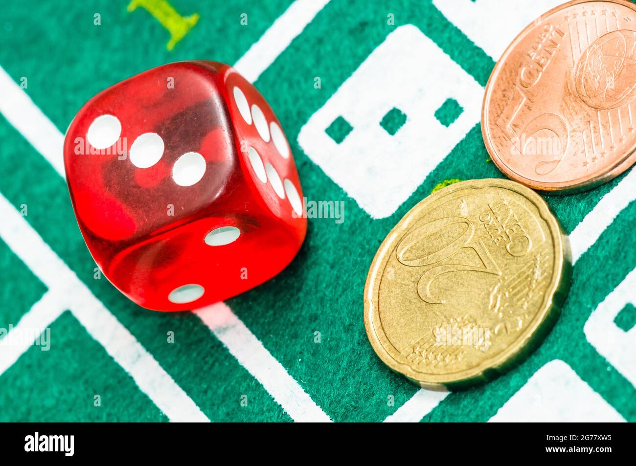 Gros plan de deux dés rouges et de pièces de 25 cents d'euros sur une planche de jeu verte Banque D'Images