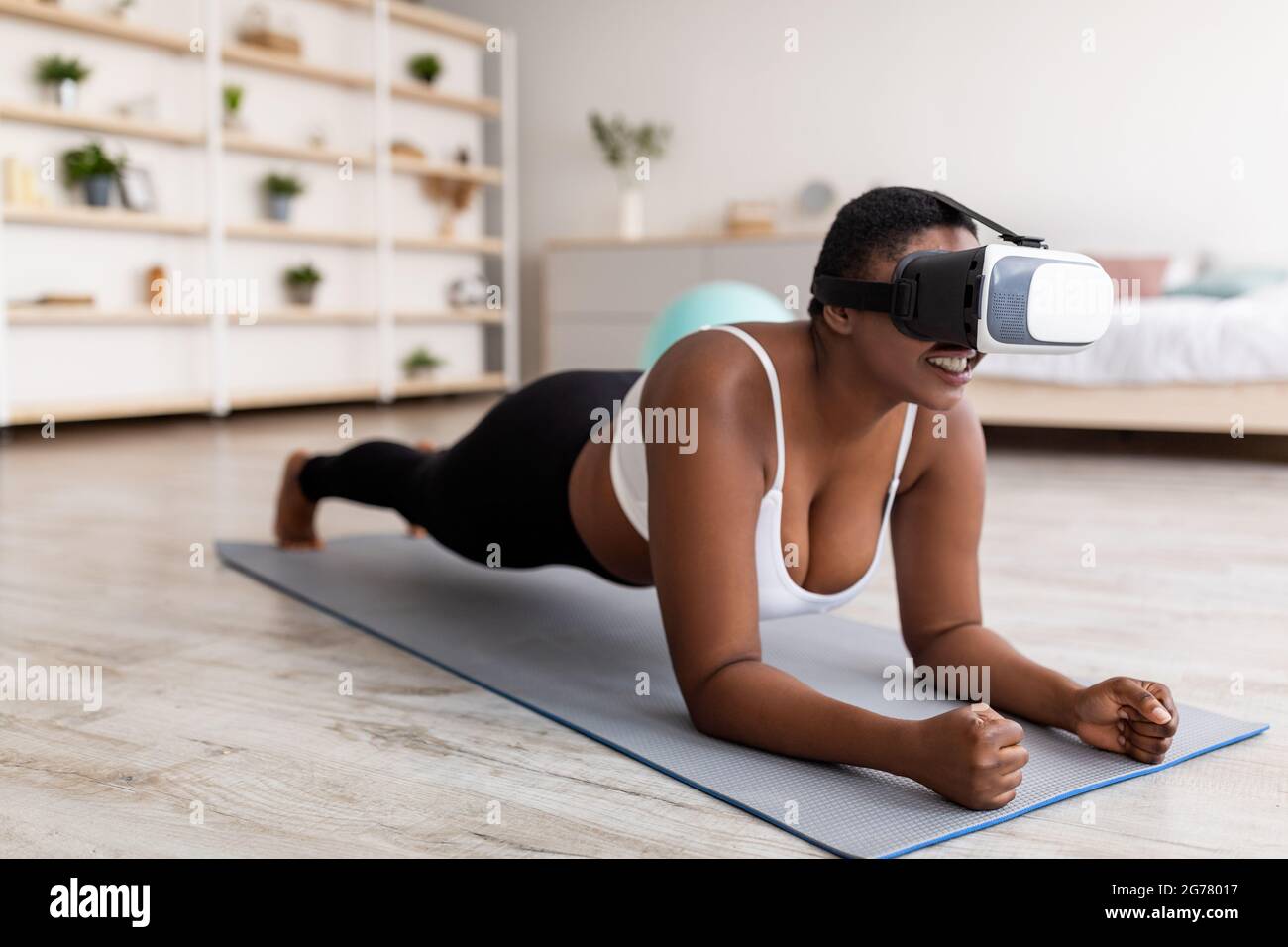 Formation virtuelle domestique. Jeune femme noire curvy en VR lunettes debout coude planche à la maison Banque D'Images
