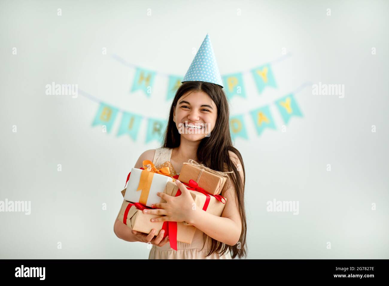 Une jeune fille indienne surjoyée dans un chapeau d'anniversaire tenant un tas de boîtes-cadeaux à l'intérieur Banque D'Images