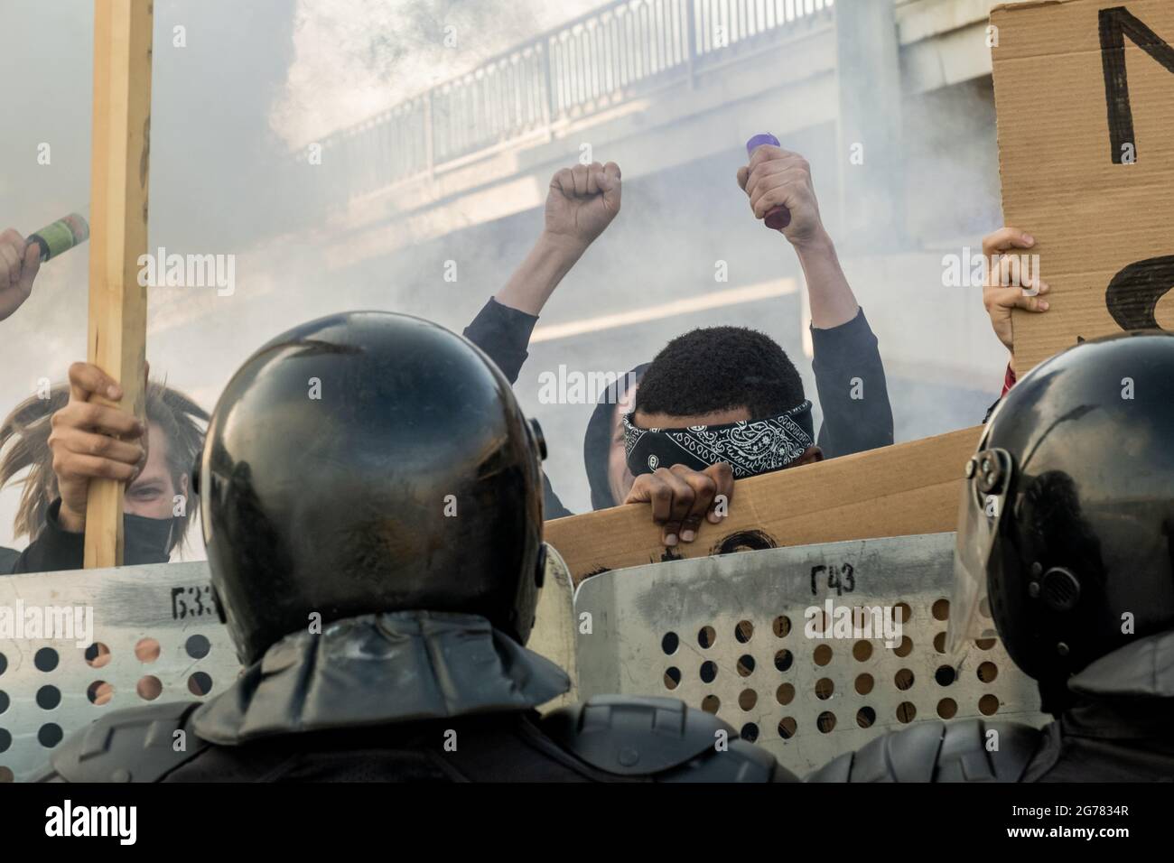 Groupe de personnes agressives avec des banderoles protestant contre l'État tandis que la police anti-émeute les tenant avec des boucliers sur des rues fumées Banque D'Images