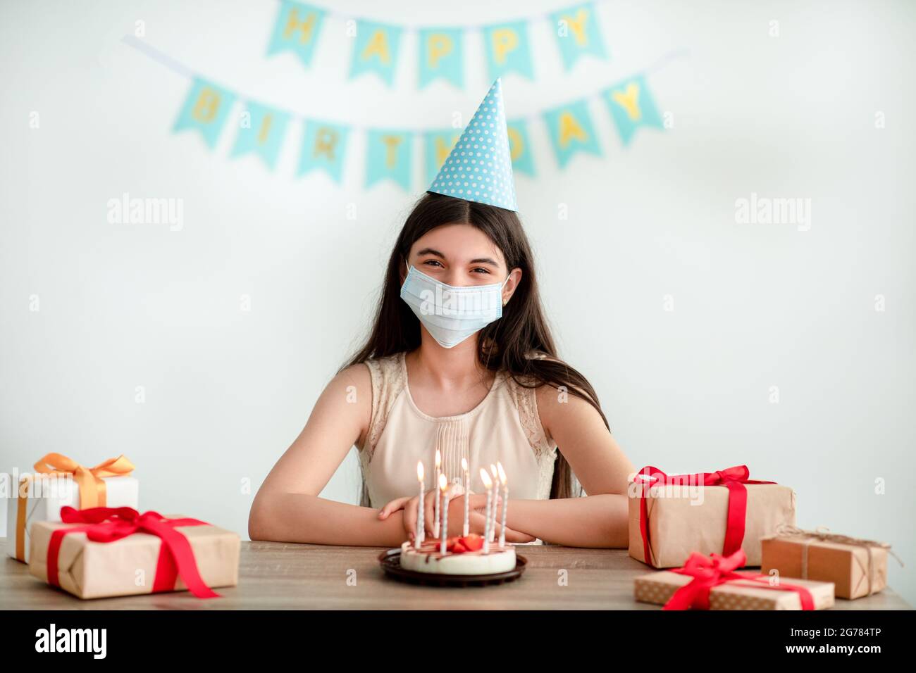 Jeune Fille Indienne En Chapeau De Fete Et Masque De Visage Assis A La Table Avec Des Boites Cadeaux Et Gateau D Anniversaire A La Maison Pendant Covid Photo Stock Alamy