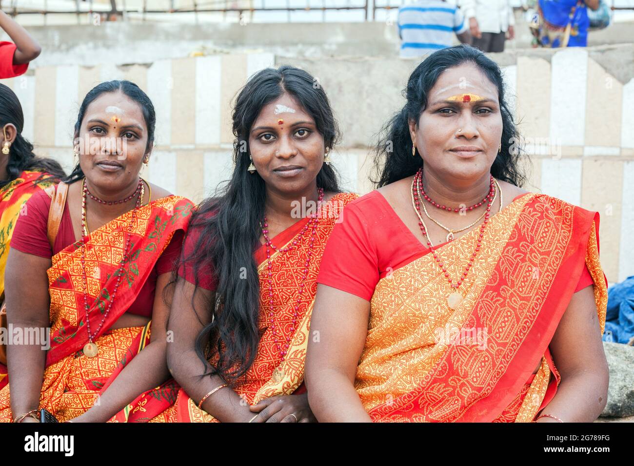 Gros plan de trois femelles indiennes portant des saris rouge/orange assis sur le mur à Kanyakumari, Tamil Nadu, Inde Banque D'Images