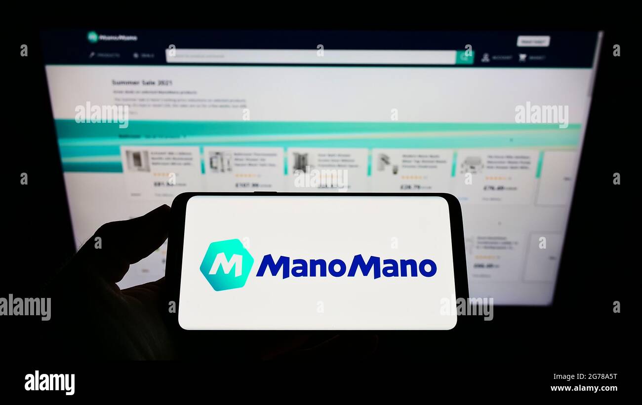 Personne tenant un téléphone portable avec le logo du marché en ligne  français ManoMano (Colibri SAS) à l'écran en face de la page Web. Mise au  point sur l'affichage du téléphone Photo