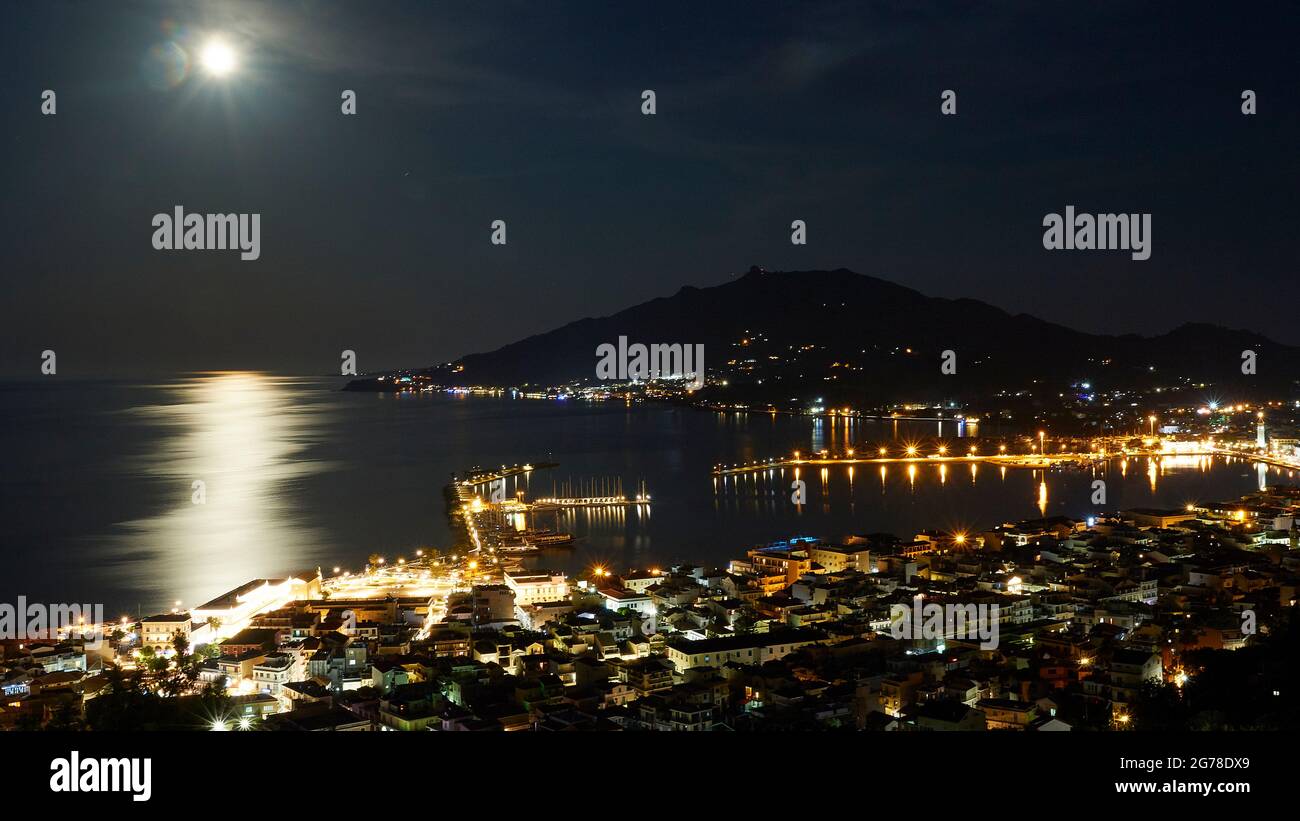 Zakynthos, Zakynthos ville, panorama de la ville depuis la colline du château, colline de Monte Yves en arrière-plan, prise de vue de nuit, pleine lune dans le coin supérieur gauche de l'image, réflexions de lune sur l'eau, ville illuminée, port éclairé Banque D'Images