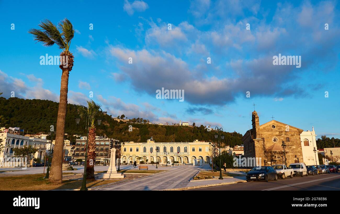 Zakynthos, ville de Zakynthos, place Solomos, palmier à gauche, Musée byzantin de Zakynthos au milieu, église Agios Nikolaos Molos à droite, lumière du matin, ciel bleu, nuages gris-blanc, gros plan Banque D'Images