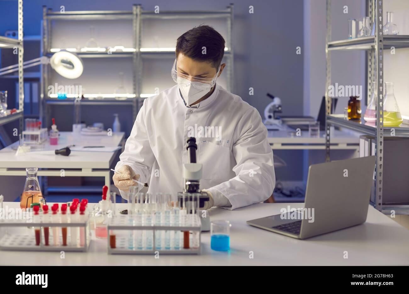Scientifique médical en masque facial et lunettes faisant des recherches en laboratoire microbiologique Banque D'Images