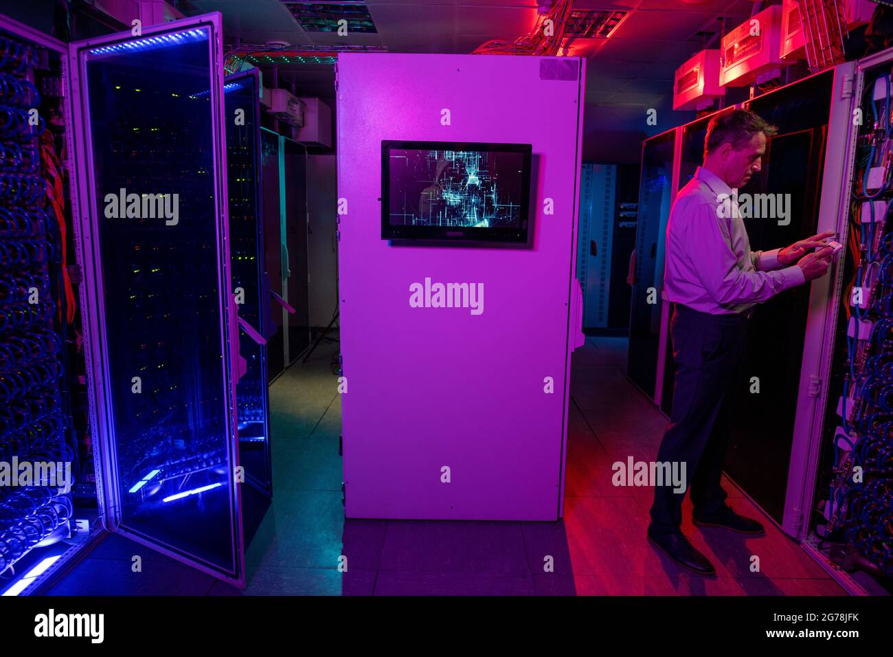 Ingénieur INFORMATIQUE mature et concentré utilisant un périphérique sans fil tout en administrant le système réseau dans un centre de données avec éclairage au néon Banque D'Images