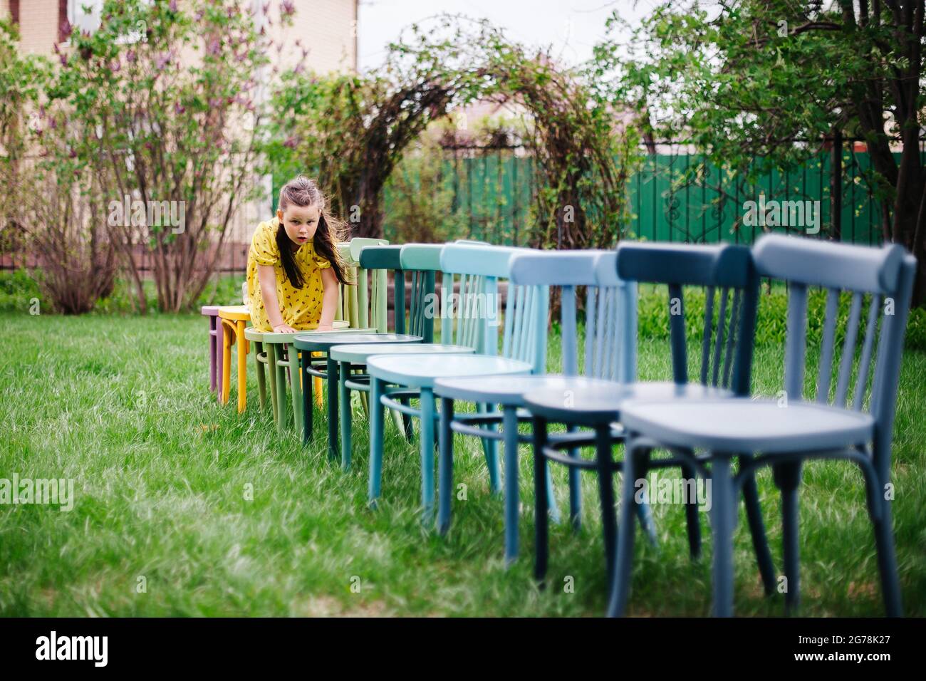 une fille rampant sur tous les fours sur une rangée de chaises en bois, préparant un mariage de terrain sur une pelouse verte dans un parc dans la nature en été Banque D'Images