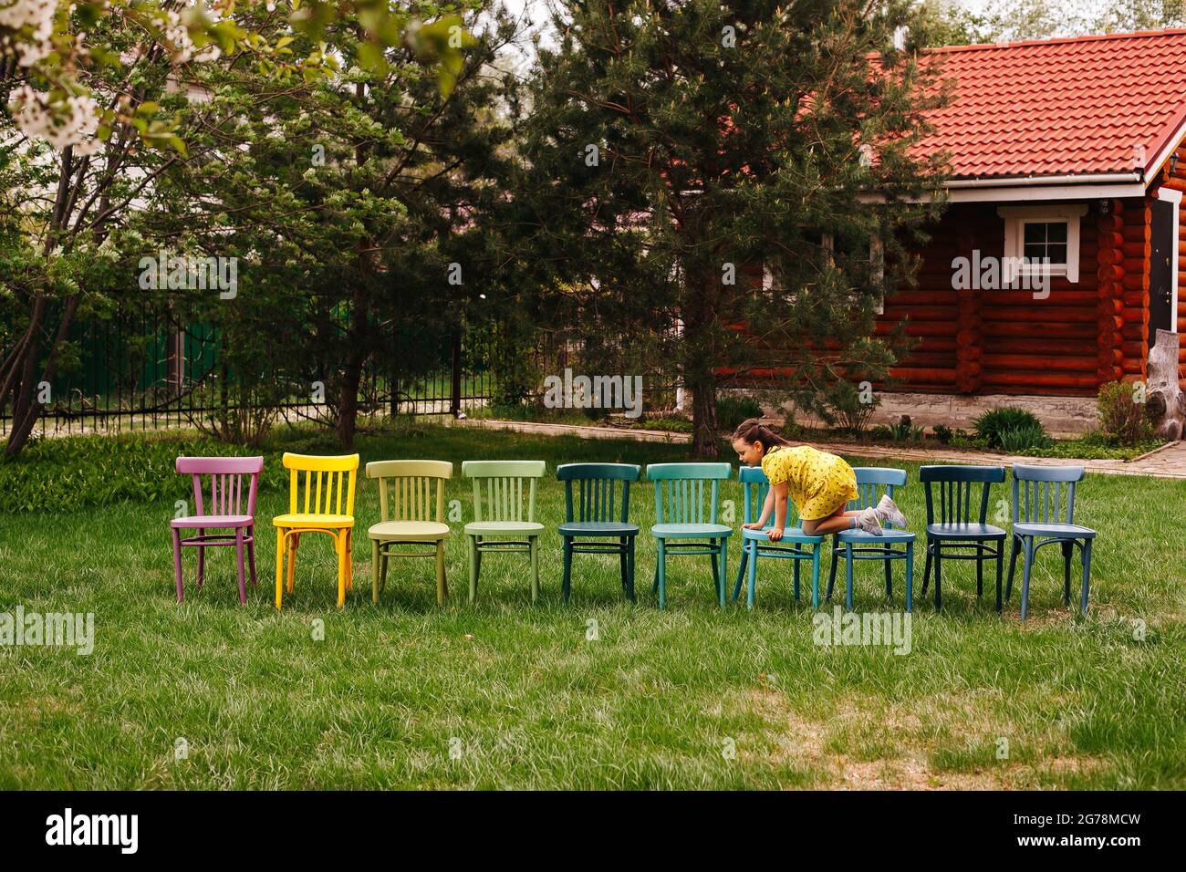 fête d'anniversaire des enfants en plein air, la fille d'anniversaire rampe le long d'une ligne de chaises colorées attendant les invités et les enfants Banque D'Images