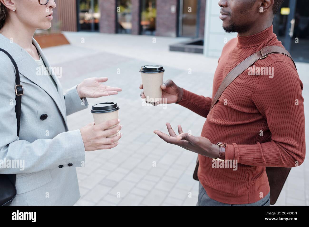 Deux jeunes collègues interculturels avec café en interaction à l'extérieur Banque D'Images