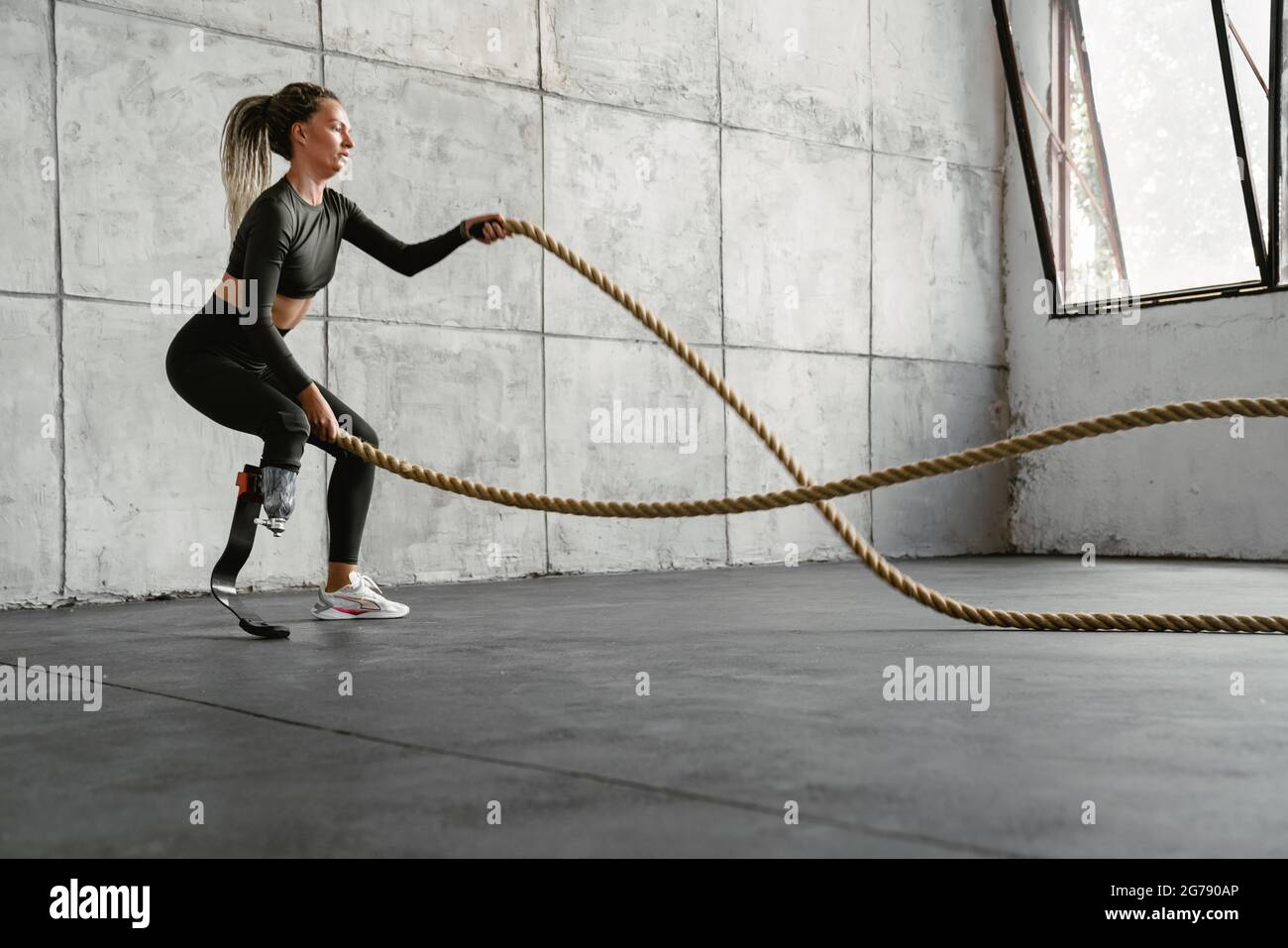 Jeune sportswoman avec prothèse, s'entraînez avec des cordes de combat à l'intérieur Banque D'Images