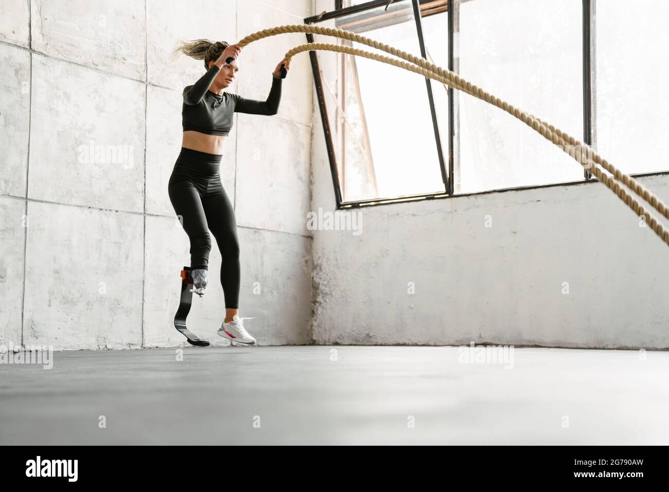 Jeune sportswoman avec prothèse, s'entraînez avec des cordes de combat à l'intérieur Banque D'Images