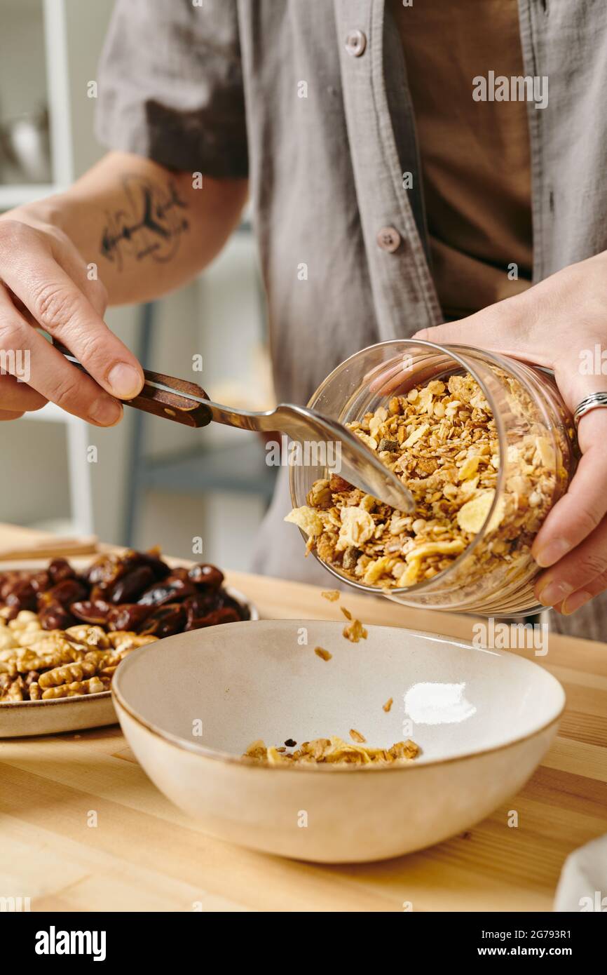 Mains de la femme mettant un peu de muesli dans le bol tout en faisant le petit déjeuner Banque D'Images