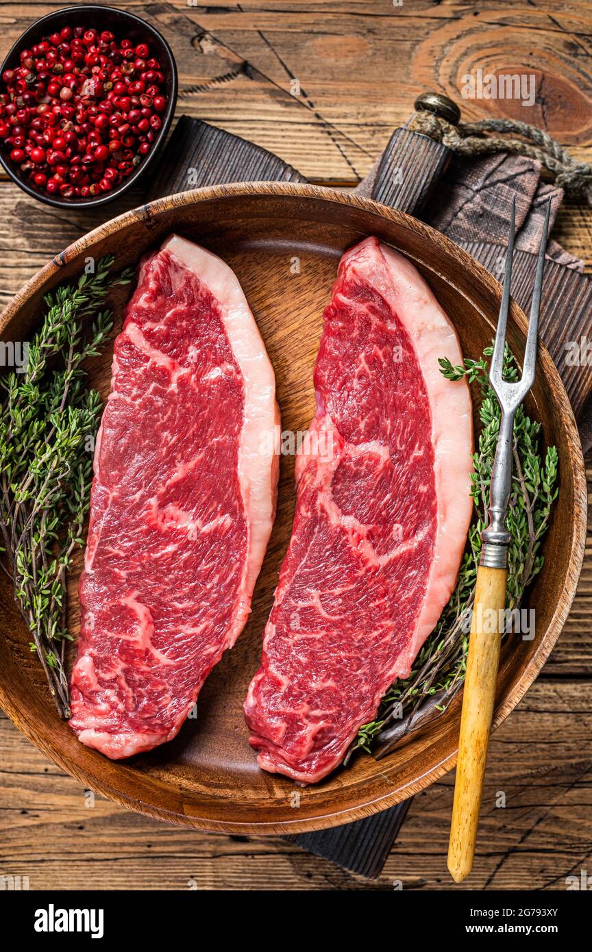 Steaks de viande de boeuf non cuits en haut cru au sommet de sirloin dans une assiette en bois avec des herbes. fond de woden. Vue de dessus Banque D'Images
