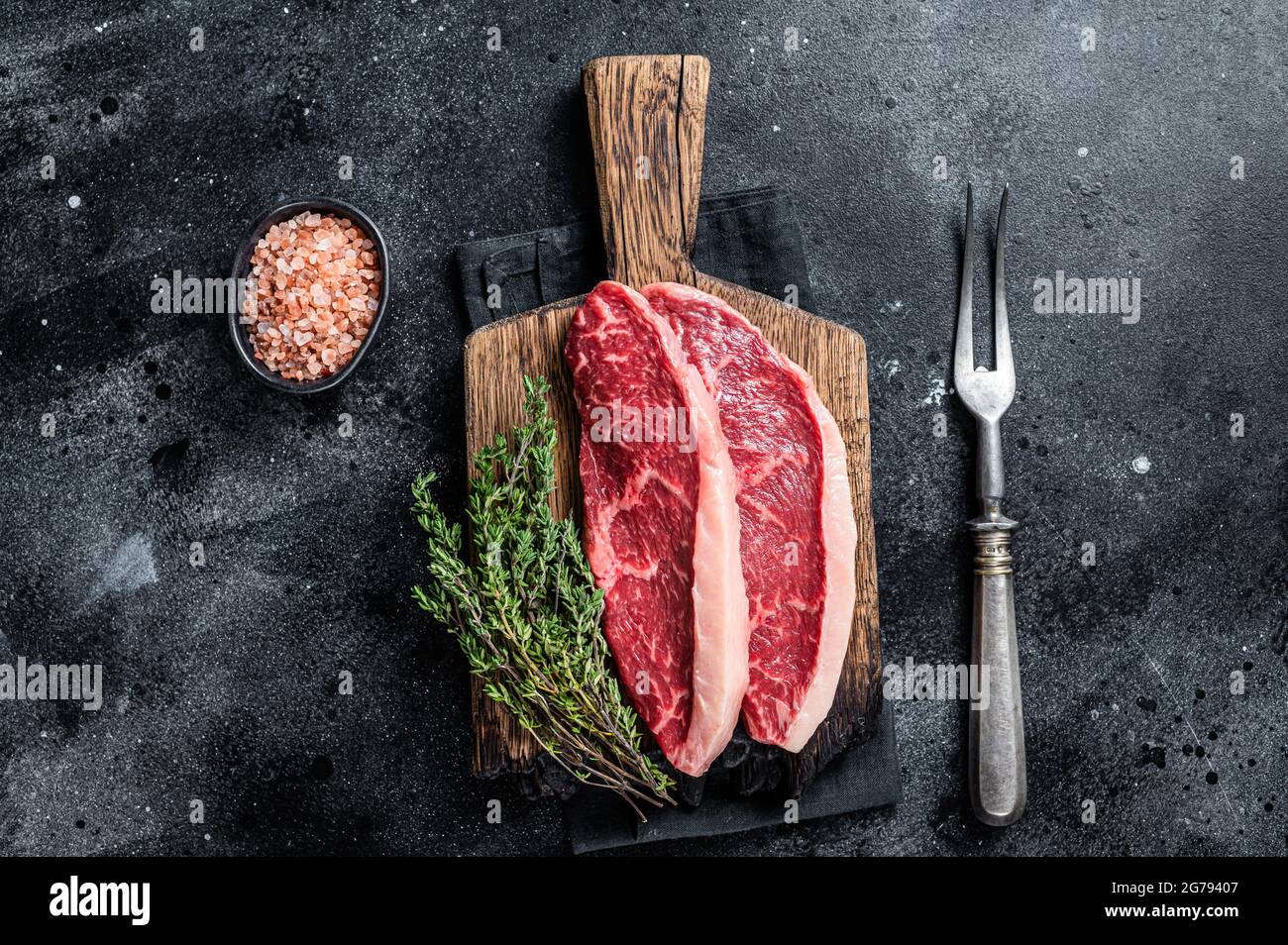 Steak de rumsteck cru non cuit ou biftecks de viande de bœuf au chapeau de sirloin sur une planche de bois. Arrière-plan noir. Vue de dessus Banque D'Images