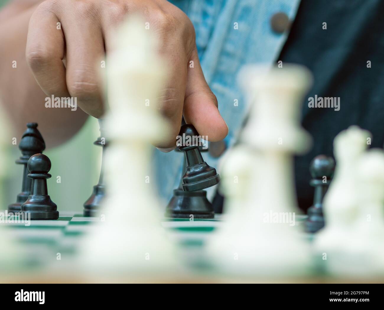 Jeu d'échecs sur un plateau vert, une main tient un pion noir Banque D'Images