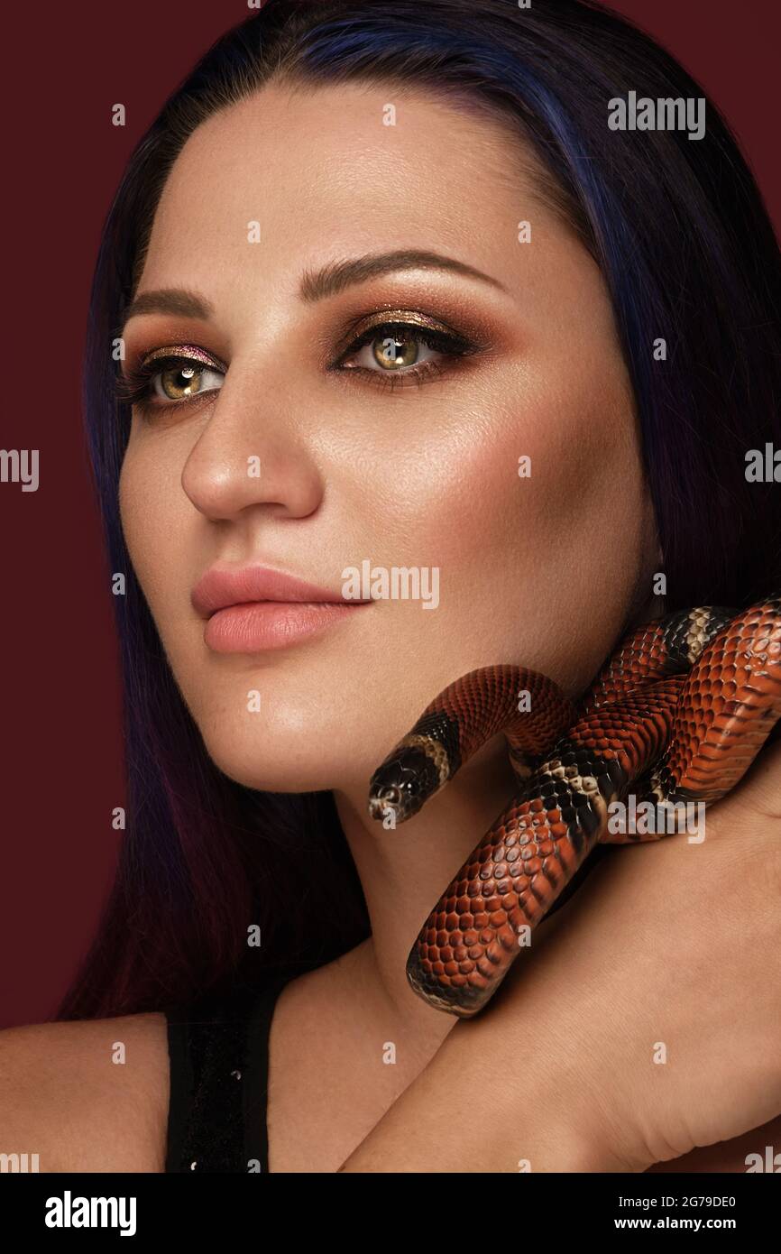 Belle fille brunette modèle avec maquillage de mode de soirée avec un serpent dans ses mains. Visage de beauté. Banque D'Images