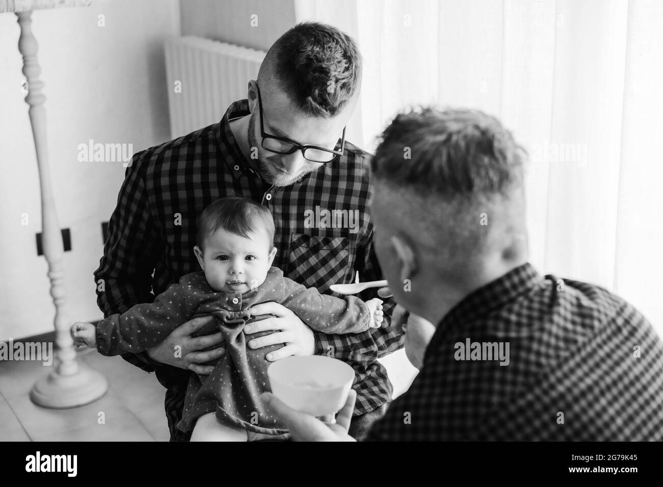 Homme gay couple avec adopté bébé fille à la maison - Deux beaux pères nourrissent la petite fille dans la cuisine - Baby-sitters masculins - famille LGBT à la maison - diversité Banque D'Images