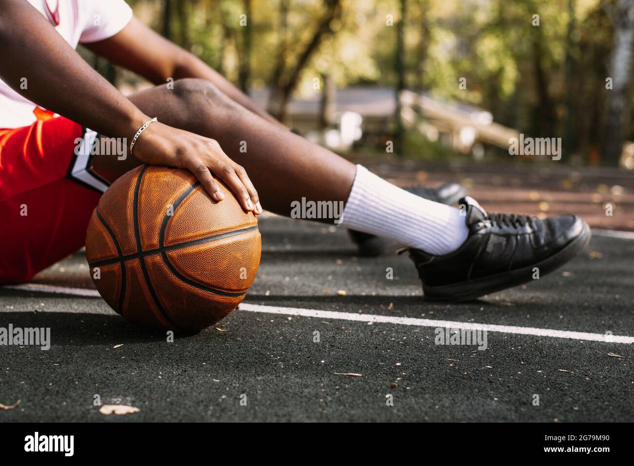 Gros plan d'un jeune homme noir tenant un ballon de basket et assis sur un terrain de basket-ball. Faites une pause pendant votre entraînement. Banque D'Images