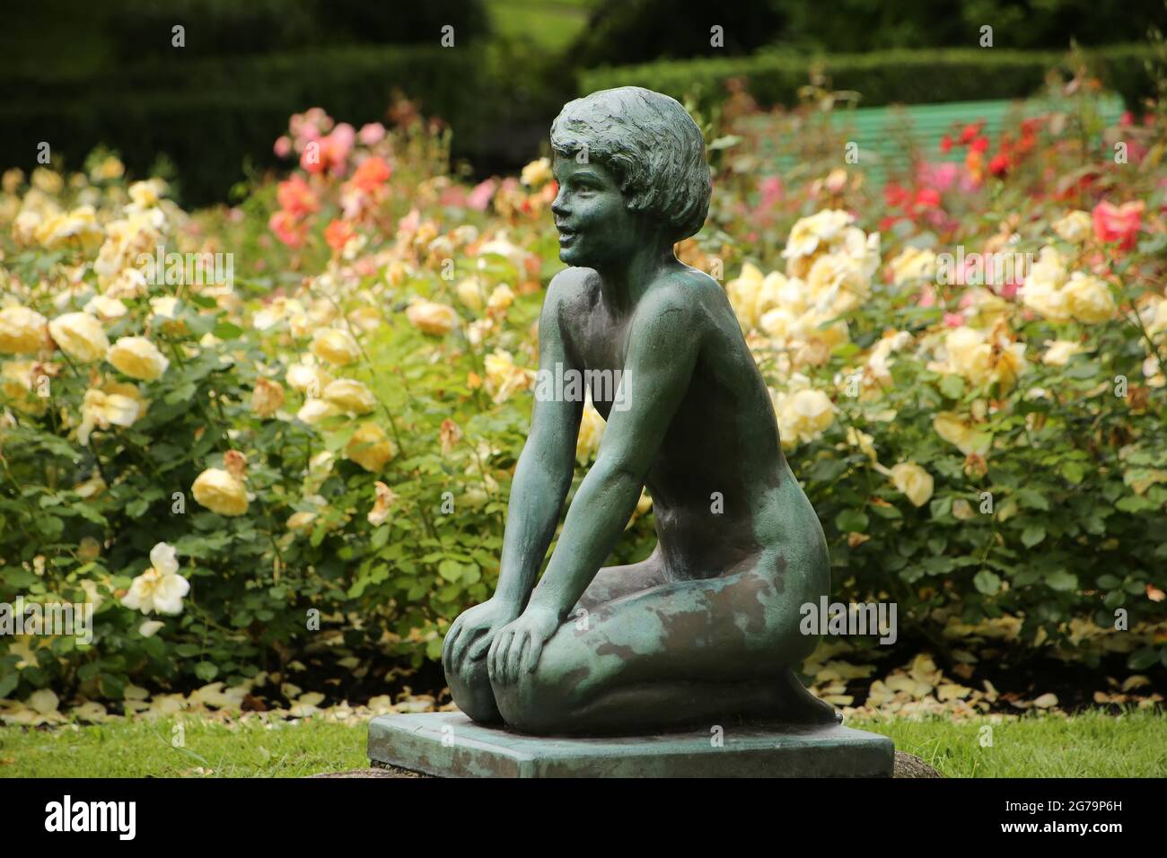 Petite sculpture ou statue d'une petite fille agenouillée entourée de plantes et d'arbres dans le centre de Byparken, Haugesund, Norvège. Banque D'Images