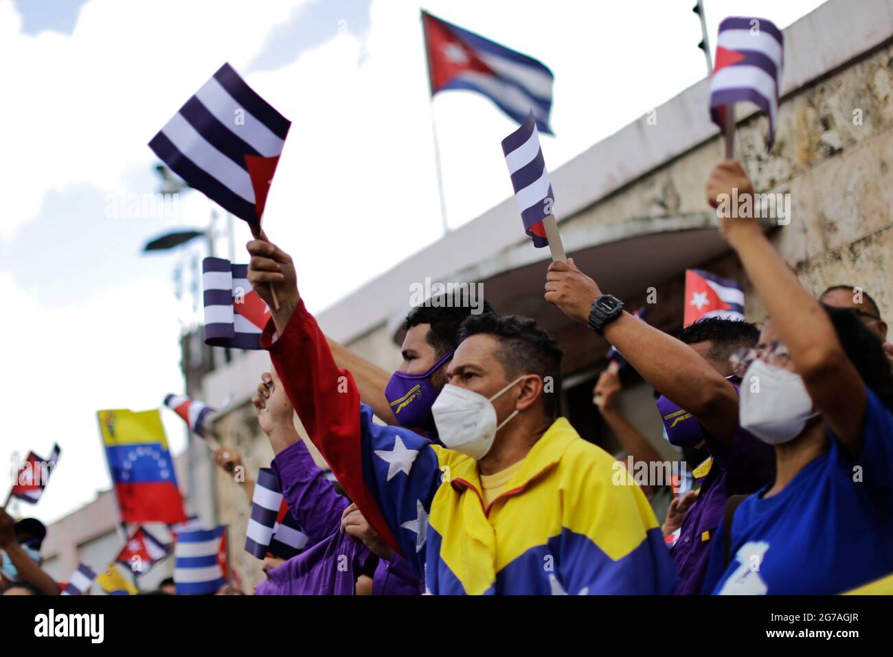 Caracas, Venezuela. 12 juillet 2021. Les manifestants qui portent la bouche tapent les drapeaux de Cuba lors d'un rassemblement devant l'ambassade de Cuba pour soutenir le gouvernement de l'île. Des dizaines de personnes avaient manifesté la veille à la Havane et dans plusieurs autres villes cubaines contre les pénuries et l'oppression. Les observateurs ont parlé des plus grandes manifestations de Cuba depuis des décennies. Credit: Jesus Vargas/dpa/Alamy Live News Banque D'Images