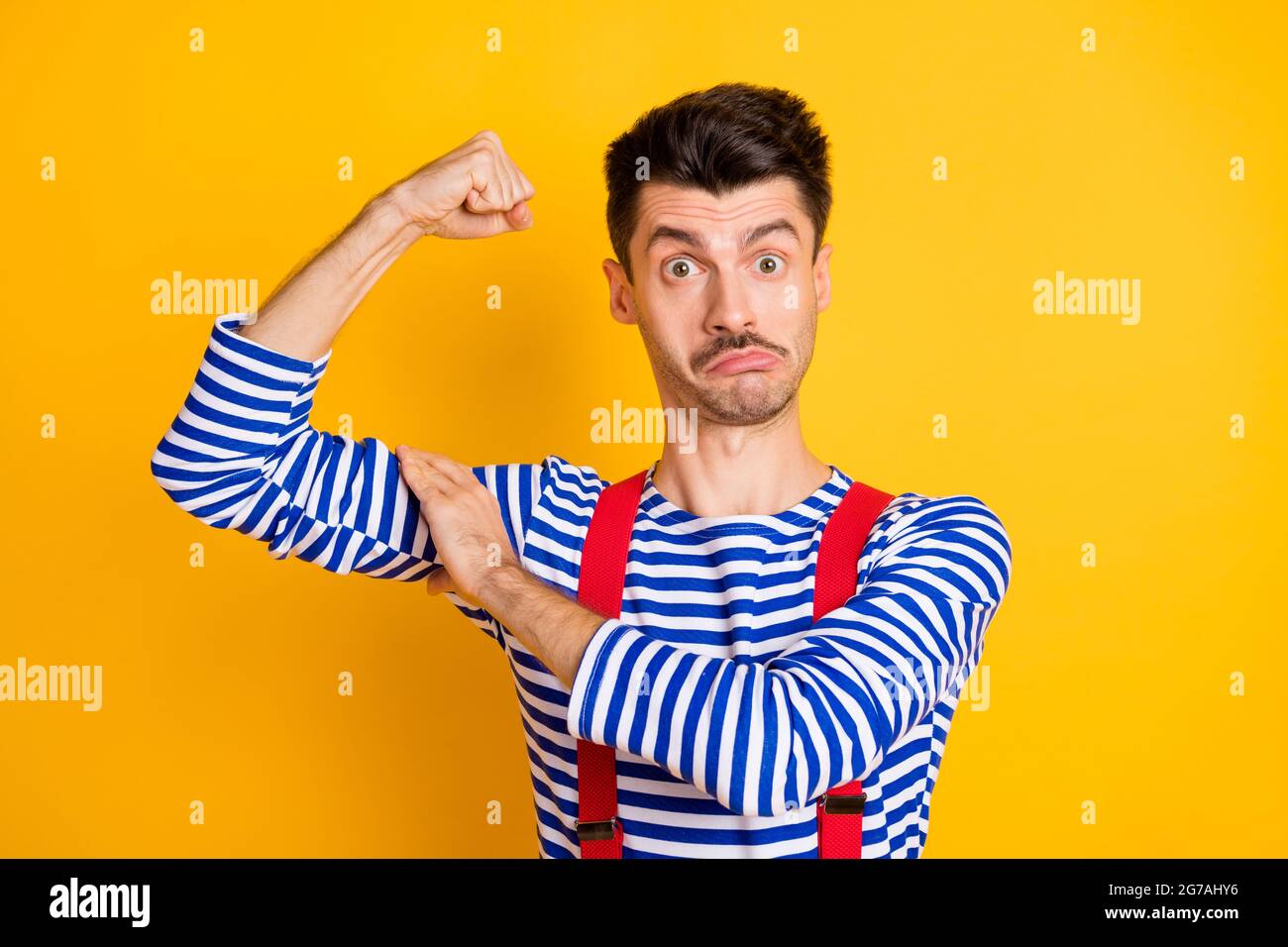 Photo de jeune funky choqué surpris homme surpris marin montrant biceps isolés sur fond jaune Banque D'Images