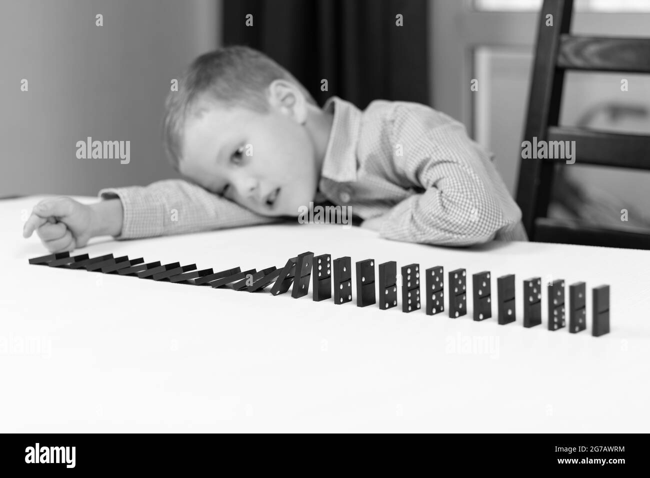 Un garçon mignon de six ans joue des dominos à la maison sur une table en bois blanc. Mise au point sélective. Gros plan Banque D'Images