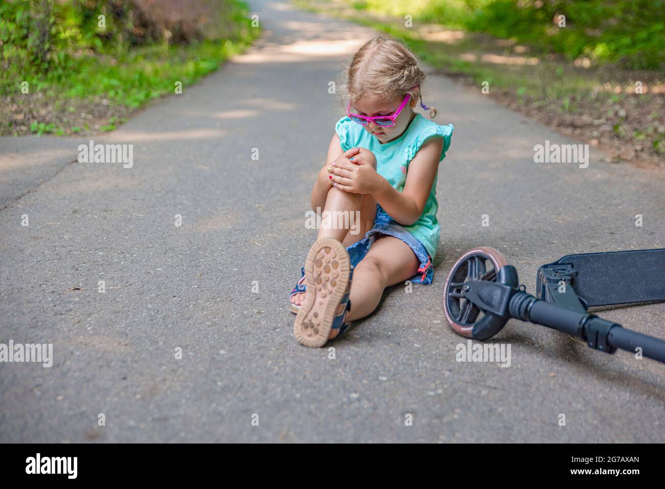 La jeune fille est tombée alors qu'elle était en scooter dans le parc et a gravement blessé son genou.Concept de blessure de scooter électrique.Prise de vue panoramique avec emplacement pour le texte Banque D'Images