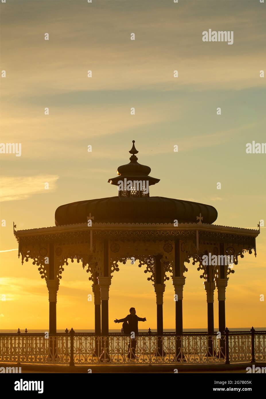 Brighton Bandstand au coucher du soleil. Brighton, East Sussex, Angleterre. Silhouette de la personne avec les bras étirés. Banque D'Images