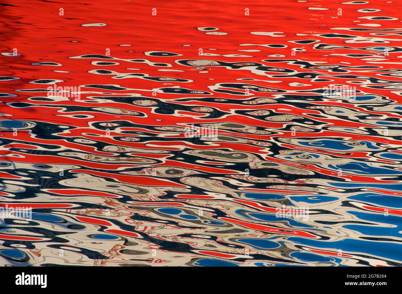 Les reflets colorés, principalement rouges dans les eaux ondulées, Marina d'Alicante, Alicante, Espagne. Banque D'Images