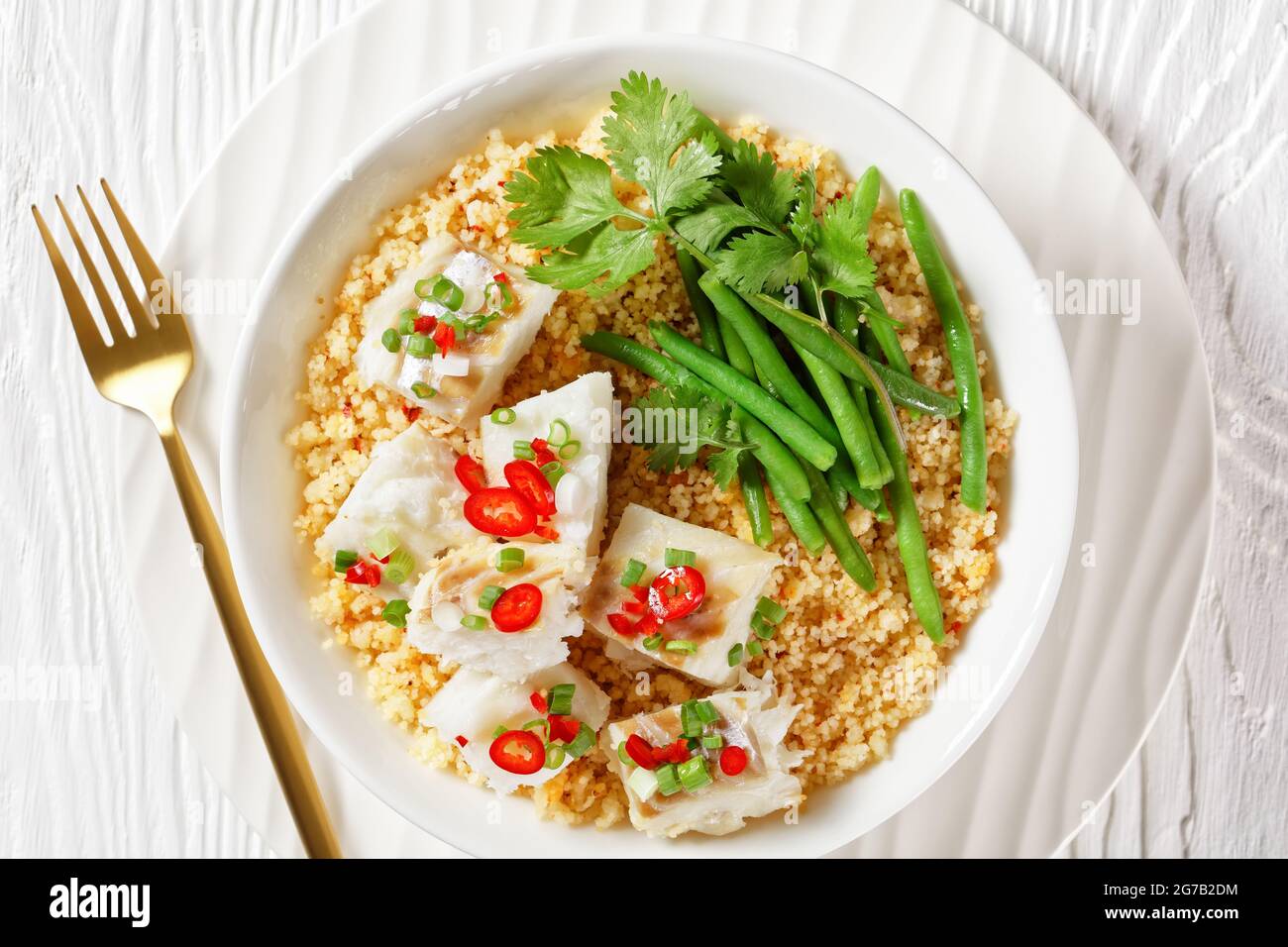 Bacalhau com todos, morue au bulgur, haricots verts cuits à la vapeur, saupoudrée de piments forts et d'oignons verts dans un bol blanc sur une table en bois, balkans Banque D'Images