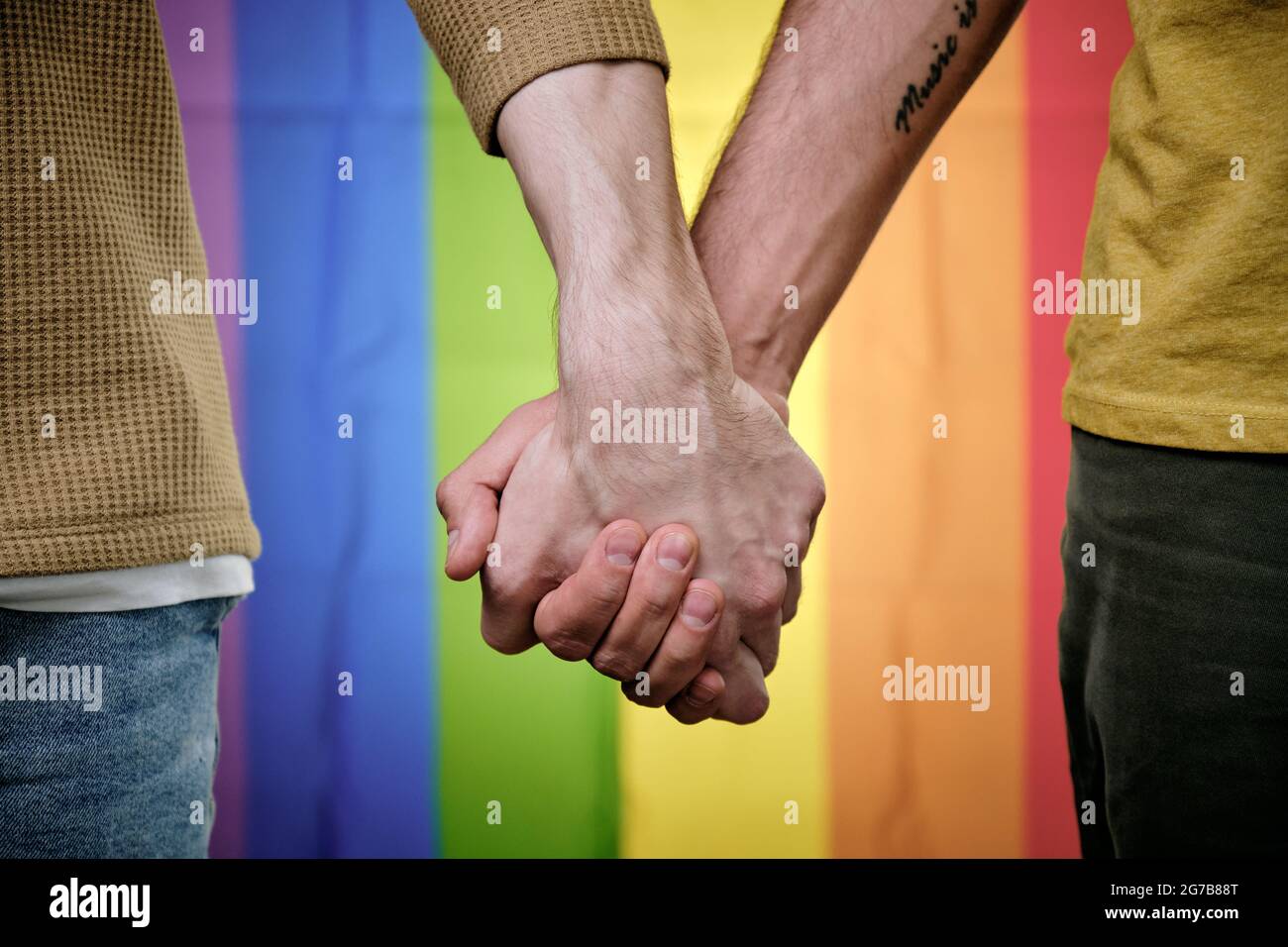 Couple gay tenant les mains en se tenant contre le drapeau arc-en-ciel LGBT Banque D'Images