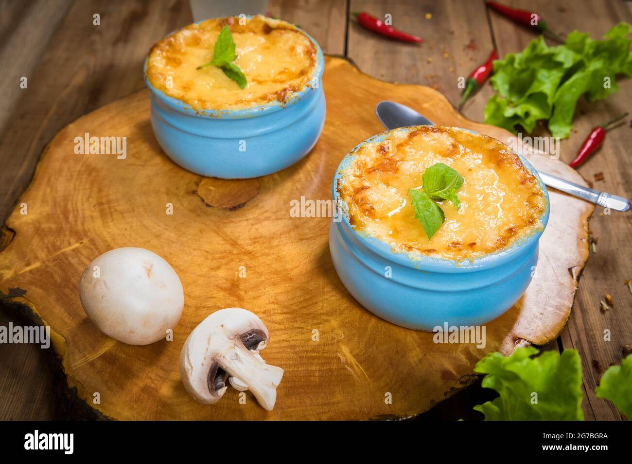 Pots avec julienne de champignons sur une planche en bois, décorés avec des herbes. Julienne à la cocotte à la croûte de fromage jaune. Banque D'Images