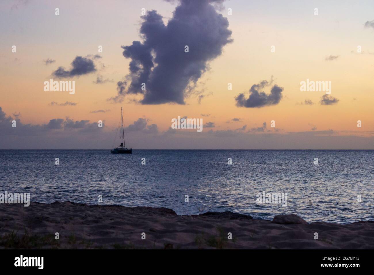 Un voilier amarré dans les Caraïbes au large de la rive près de Frederiksted, Sainte Croix, USVI comme le coucher du soleil se reflète dans les nuages et la mer. Banque D'Images