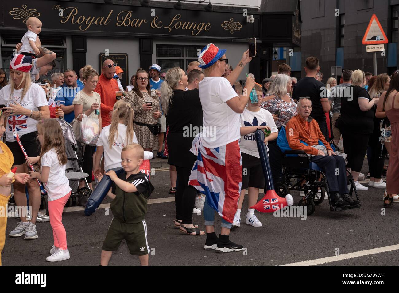 Les spectateurs se rassemblent pour assister à la marche Orange sur Shankill Road, un quartier majoritairement loyaliste. Chaque été, à l'exception de l'année dernière en raison du Covid-19, les manifestants défilent dans les rues de Belfast pour les défilés du 12 juillet/Marche Orange pour célébrer la bataille de la Boyne. Les marches orange ont rencontré des critiques tout au long de l'existence de l'ordre, des catholiques et des nationalistes, qui les perçoivent comme sectaires et triomphalistes. Malgré un passé de désordre public pendant les défilés, ainsi que le mécontentement et la frustration protestants dus aux récents accords du Brexit, le défilé a été ca Banque D'Images