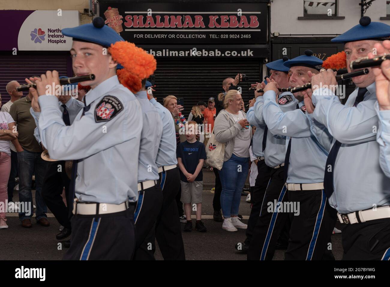 Les spectateurs regardent et applaudissent les membres du groupe jouant de la flûte sur Shankill Road, un quartier majoritairement loyaliste.chaque été, à l'exception de l'année dernière en raison du Covid-19, les manifestants défilent dans les rues de Belfast pour les défilés du 12 juillet/Marche orange pour célébrer la bataille de la Boyne. Les marches orange ont rencontré des critiques tout au long de l'existence de l'ordre, des catholiques et des nationalistes, qui les perçoivent comme sectaires et triomphalistes. Malgré un passé de désordre public pendant les défilés, ainsi que le mécontentement et la frustration protestants dus aux récents accords sur le Brexit, Banque D'Images