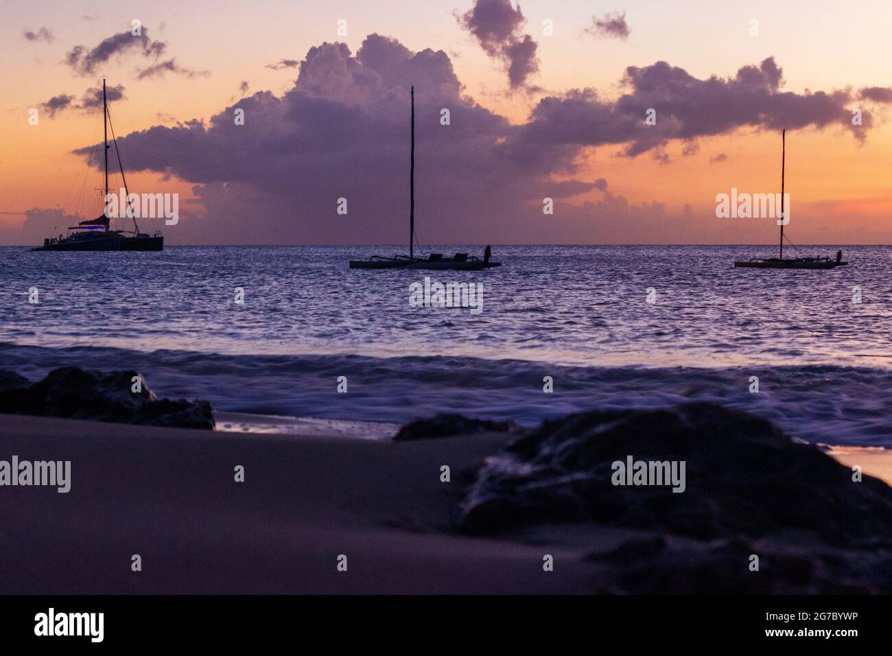 Trois voiliers amarrés dans les Caraïbes au large de la rive près de Frederiksted, Sainte Croix, USVI comme le coucher du soleil se reflète dans les nuages et la mer. Banque D'Images