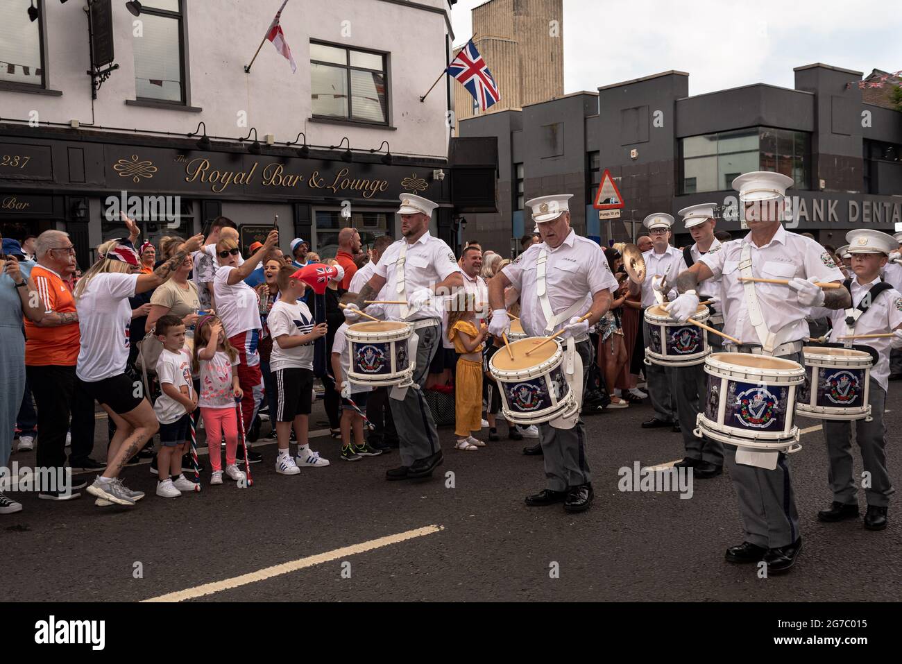 Les spectateurs regardent et applaudissent les membres du groupe jouant des tambours sur Shankill Road, un quartier majoritairement loyaliste.chaque été, à l'exception de l'année dernière en raison du Covid-19, les manifestants défilent dans les rues de Belfast pour le douzième juillet des défilés/la marche Orange pour célébrer la bataille de la Boyne. Les marches orange ont rencontré des critiques tout au long de l'existence de l'ordre, des catholiques et des nationalistes, qui les perçoivent comme sectaires et triomphalistes. Malgré un passé de désordre public pendant les défilés, ainsi que le mécontentement et la frustration protestants dus aux récents accords sur le Brexit, Banque D'Images