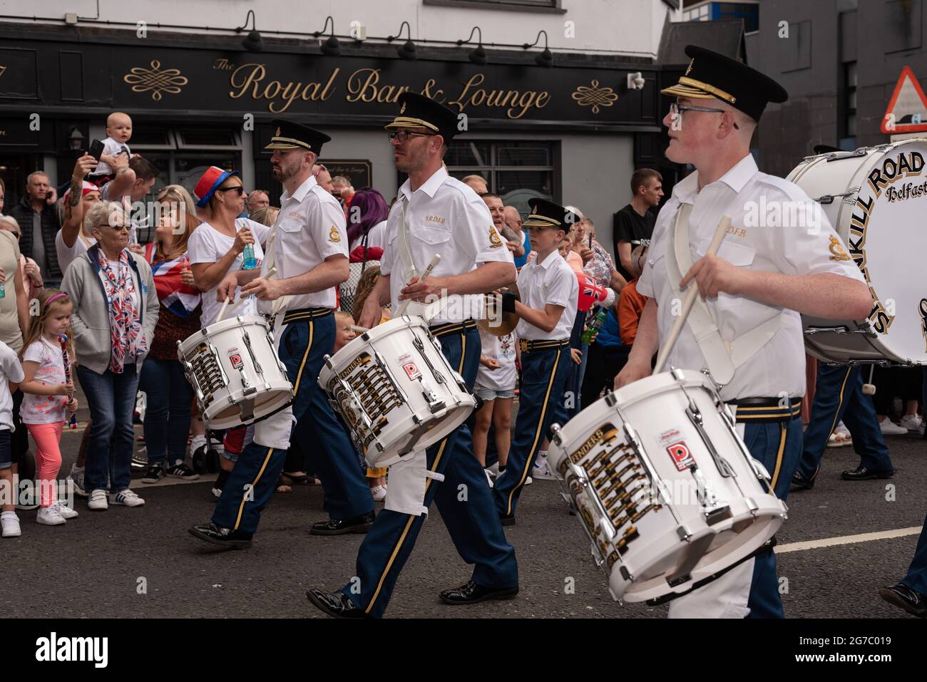 Les spectateurs regardent et applaudissent les membres du groupe jouant des tambours sur Shankill Road, un quartier majoritairement loyaliste.chaque été, à l'exception de l'année dernière en raison du Covid-19, les manifestants défilent dans les rues de Belfast pour le douzième juillet des défilés/la marche Orange pour célébrer la bataille de la Boyne. Les marches orange ont rencontré des critiques tout au long de l'existence de l'ordre, des catholiques et des nationalistes, qui les perçoivent comme sectaires et triomphalistes. Malgré un passé de désordre public pendant les défilés, ainsi que le mécontentement et la frustration protestants dus aux récents accords sur le Brexit, Banque D'Images
