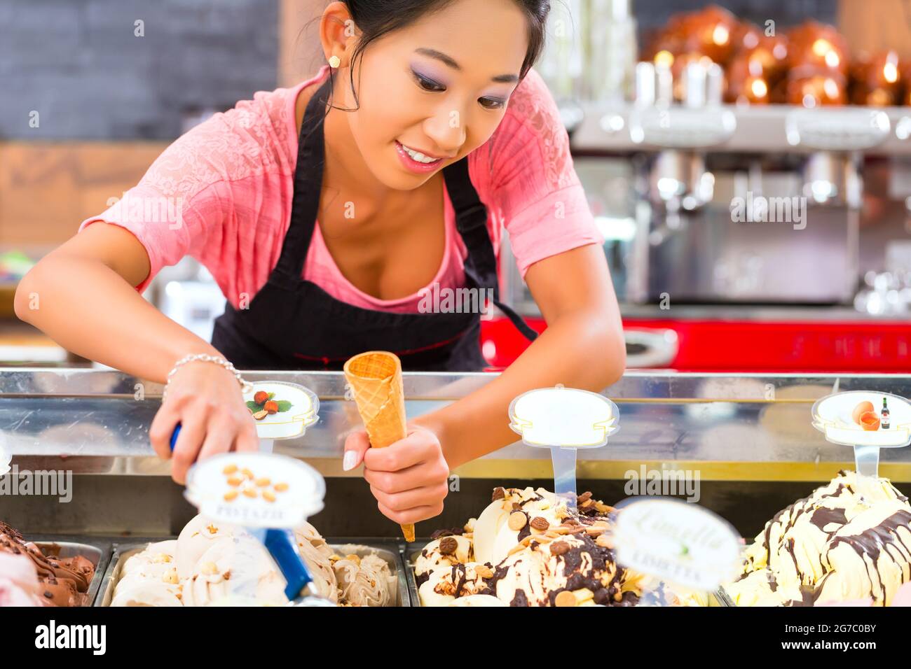Jeune vendeuse asiatique dans un glacier prend une boule de crème glacée Banque D'Images