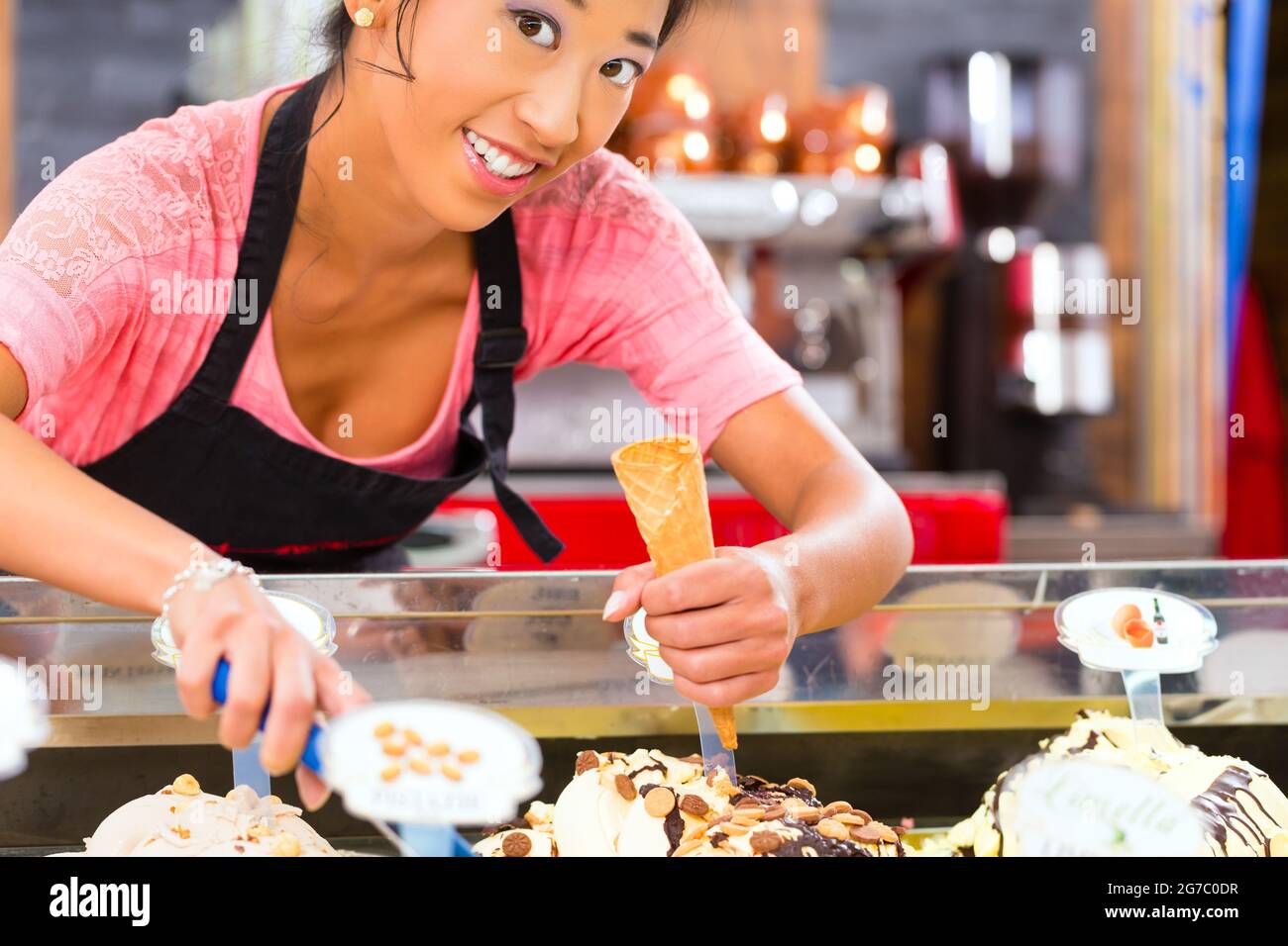 Jeune vendeuse asiatique dans un glacier prend une boule de crème glacée Banque D'Images