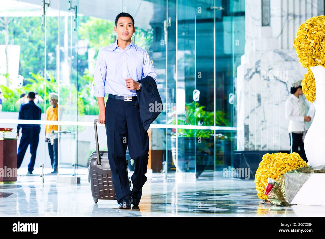 Asian man pulling suitcase in hotel lobby Banque D'Images