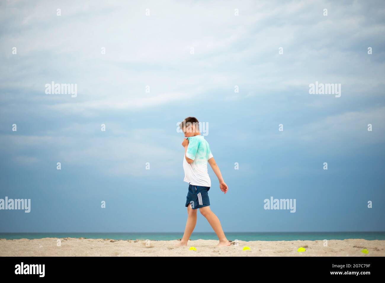 Entraînement de garçon sur une plage de sable. Des balles de tennis sont réparties sur la côte. Repos entre les exercices. Banque D'Images