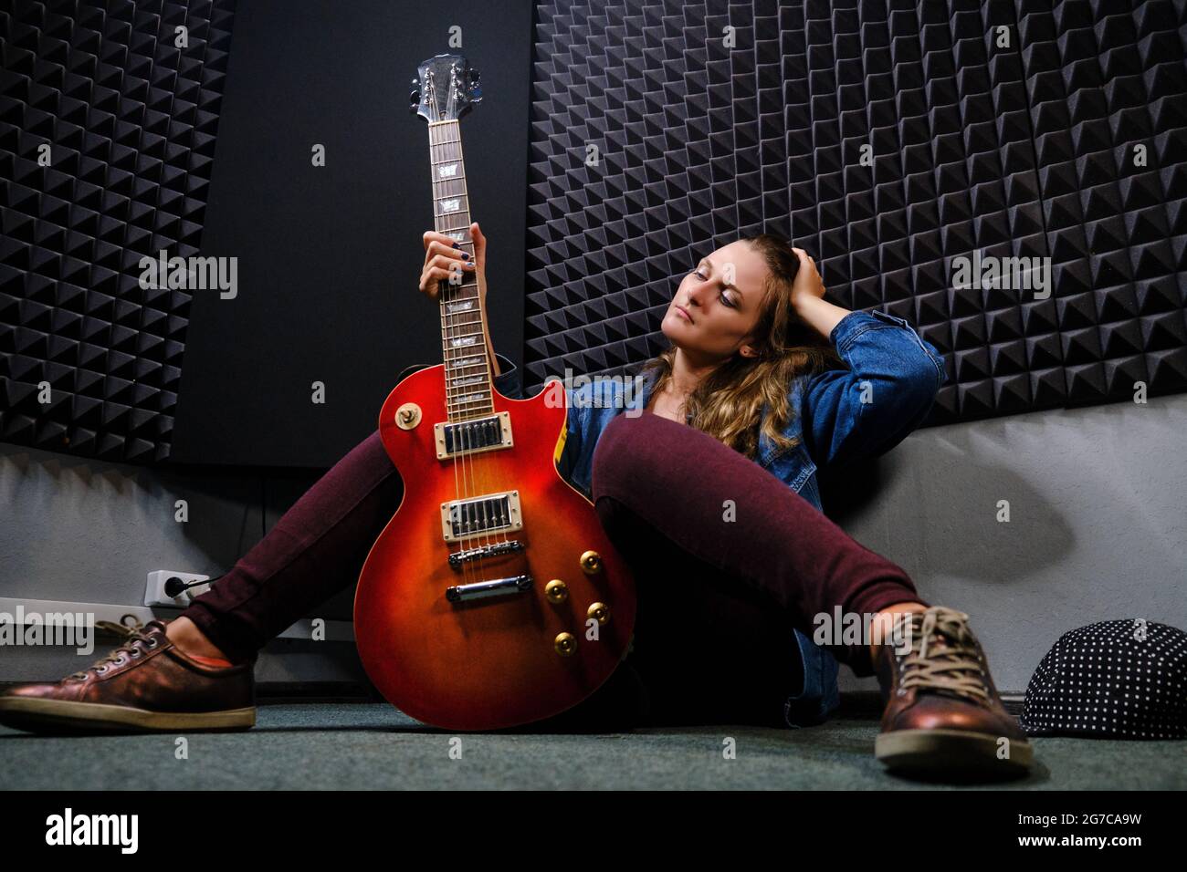 Une jeune femme assise sur le sol avec une guitare électrique dans le  studio d'enregistrement. Guitariste avec une belle guitare rouge.  Enregistrement professionnel de mus Photo Stock - Alamy